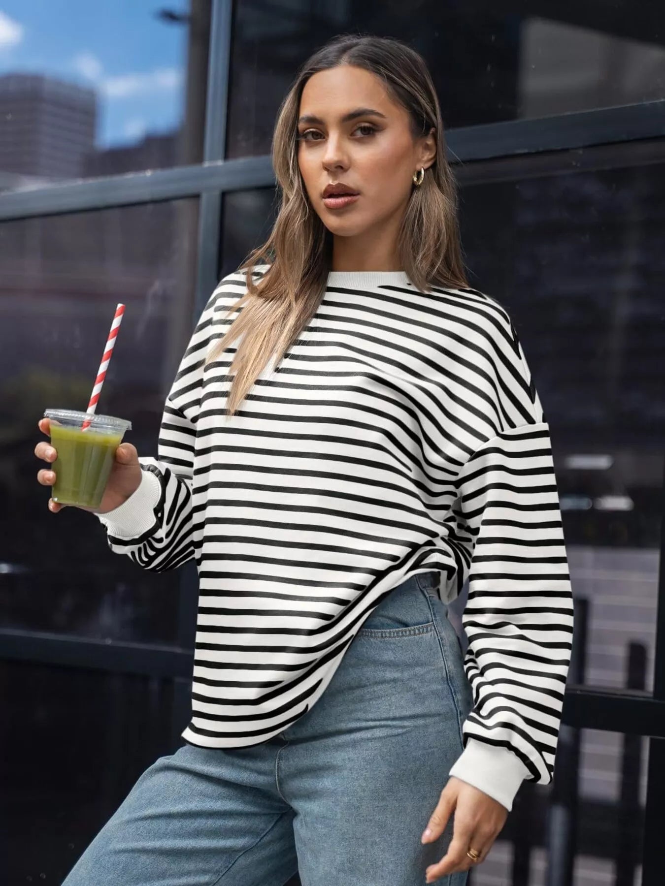 Woman in a striped sweater holding a green smoothie in an urban setting