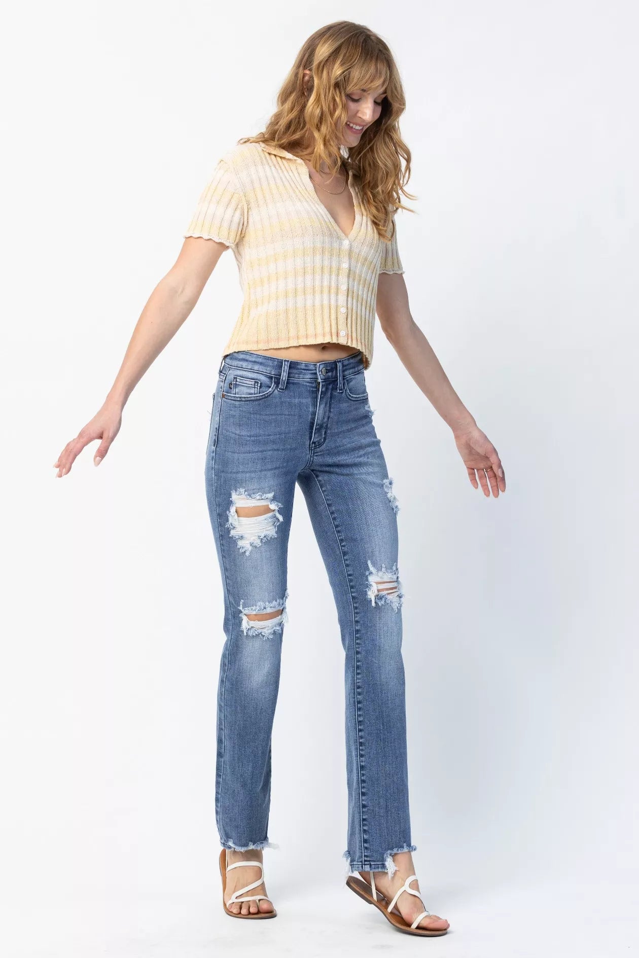 Woman wearing a yellow striped shirt and blue ripped jeans on a white background