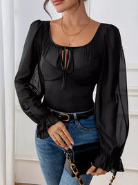 Person wearing a black blouse with long sleeves and blue jeans against a white background
