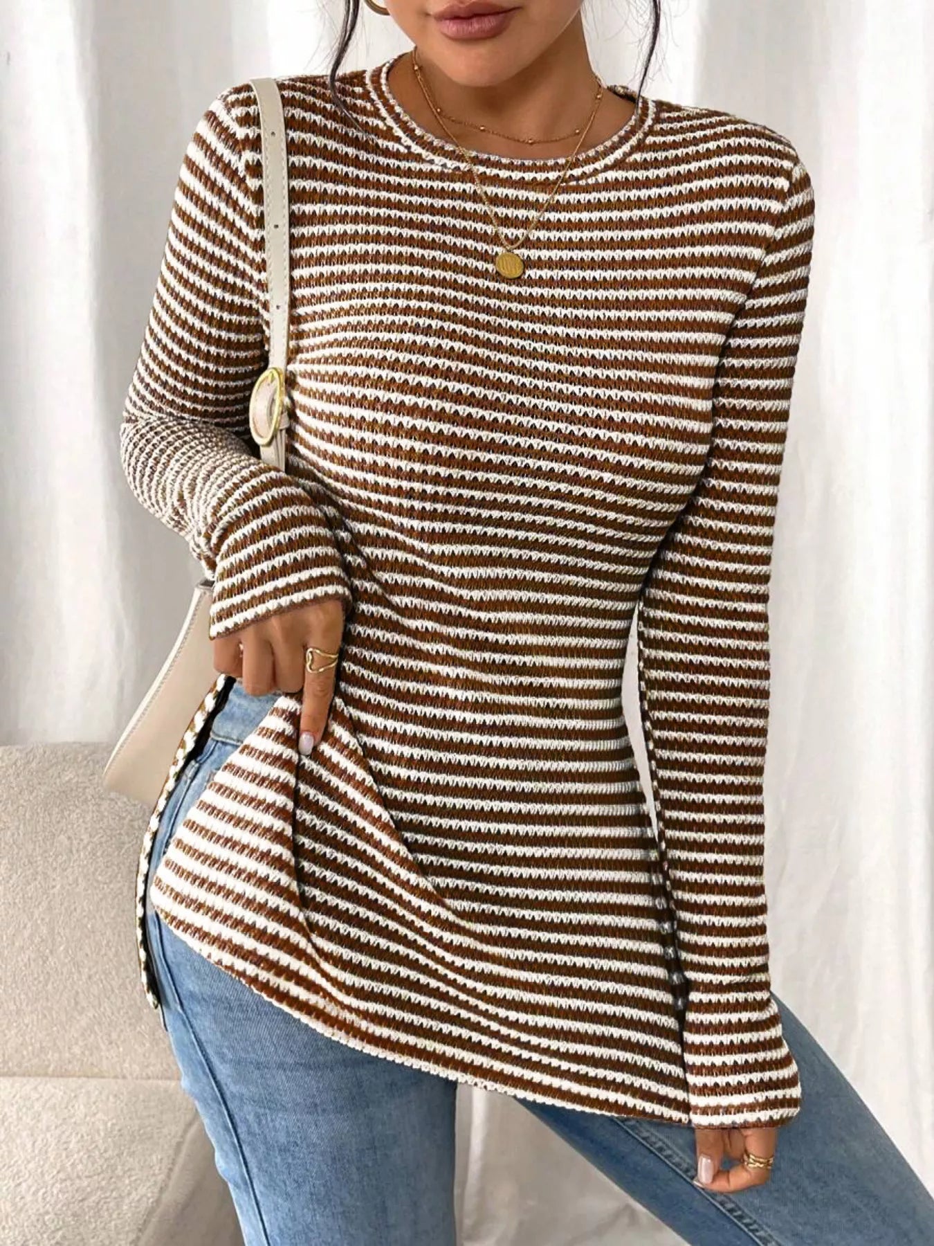 Person wearing a brown and beige striped long-sleeve top with blue jeans against a neutral background
