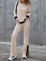 Person wearing a beige ribbed sweater and pants set with black accents against a gray concrete wall.