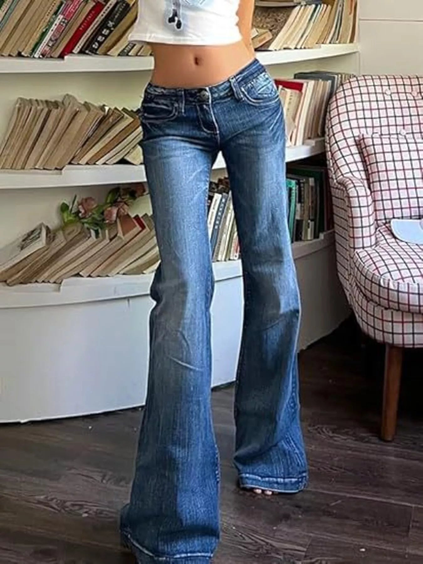 Person wearing blue flared jeans standing in a room with bookshelves and a chair.