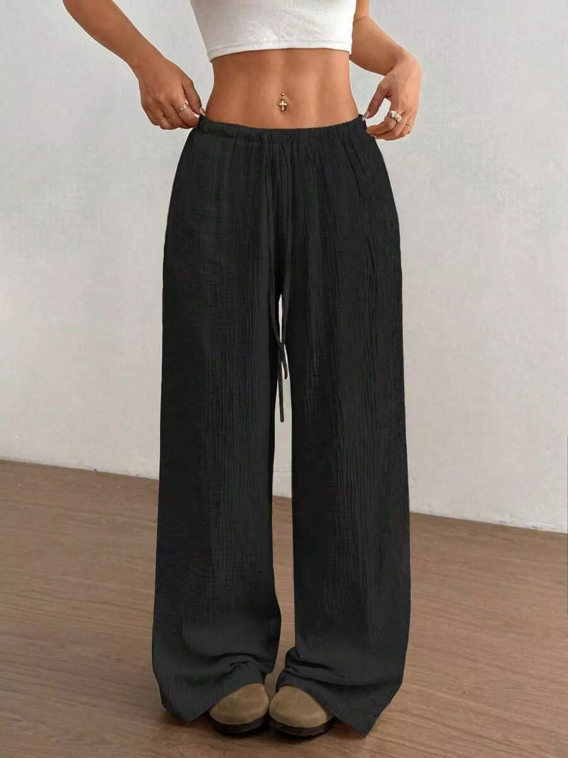 Person wearing black wide-leg pants and a white top against a plain background