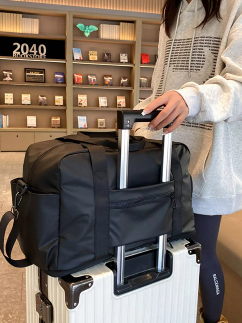 Person holding a black duffel bag over a white suitcase in a store setting.