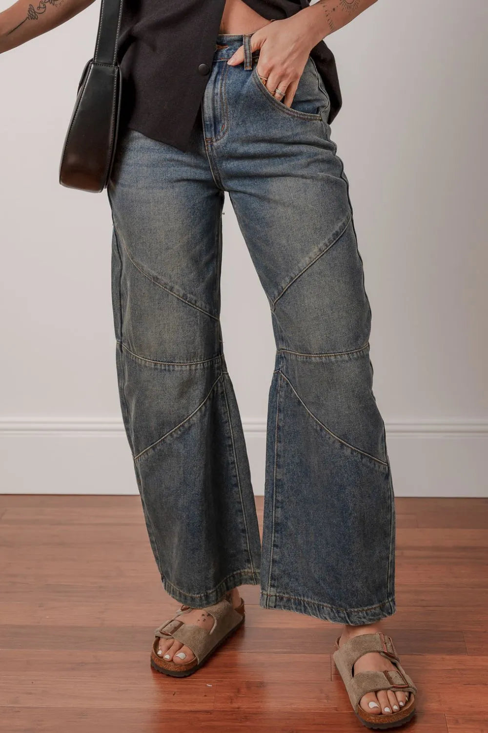 Person wearing wide-leg jeans and sandals on a wooden floor.