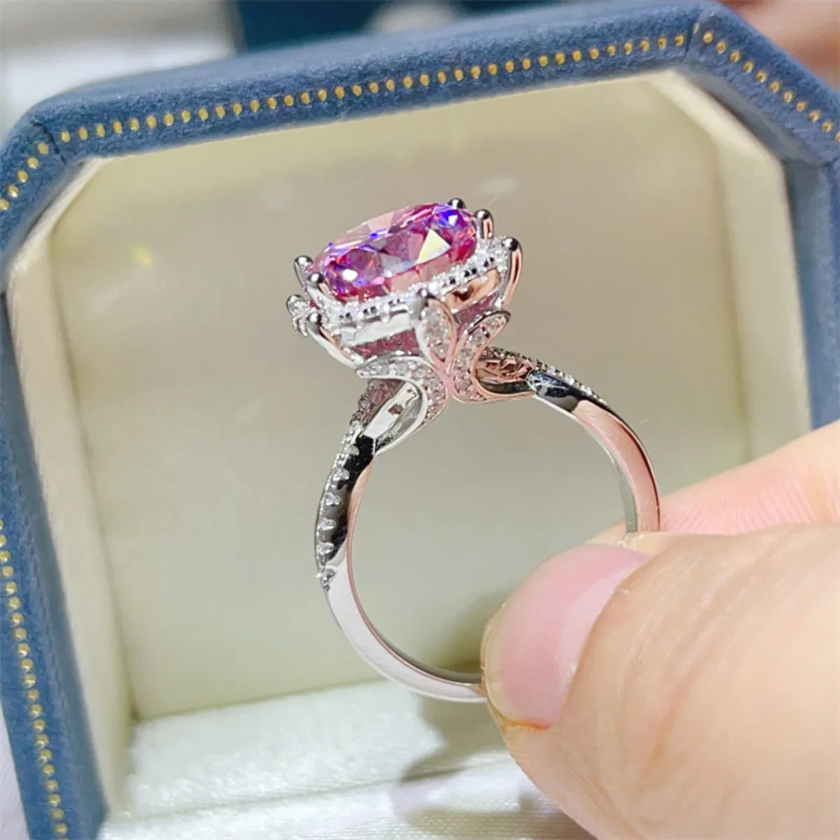 Rose gold ring with pink gemstone held by a hand, set against a soft focus background.