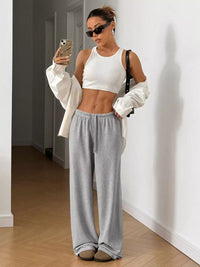 Woman taking a mirror selfie wearing a white top and gray sweatpants indoors.