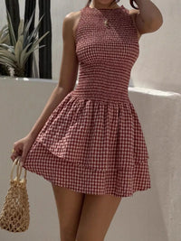 Woman wearing a red and white checkered dress holding a straw bag against a neutral background