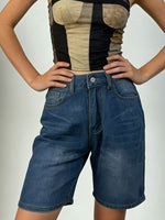 Person wearing a black and beige top with denim shorts on a plain background