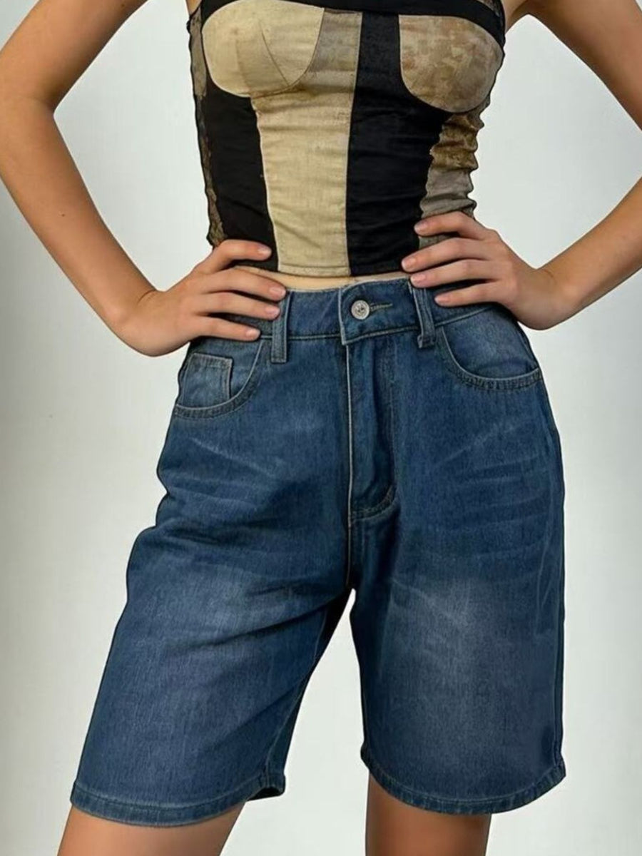 Person wearing a black and beige top with denim shorts on a plain background