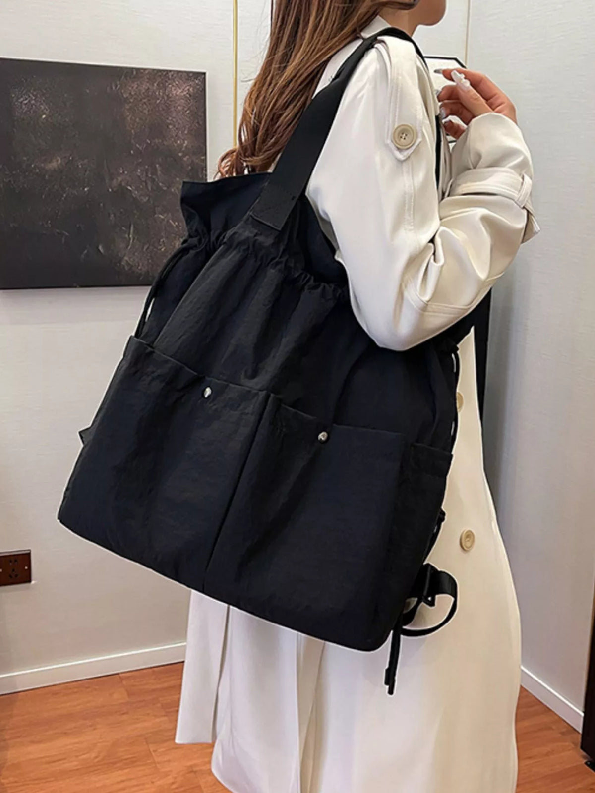 Person wearing a black backpack indoors against a plain wall.