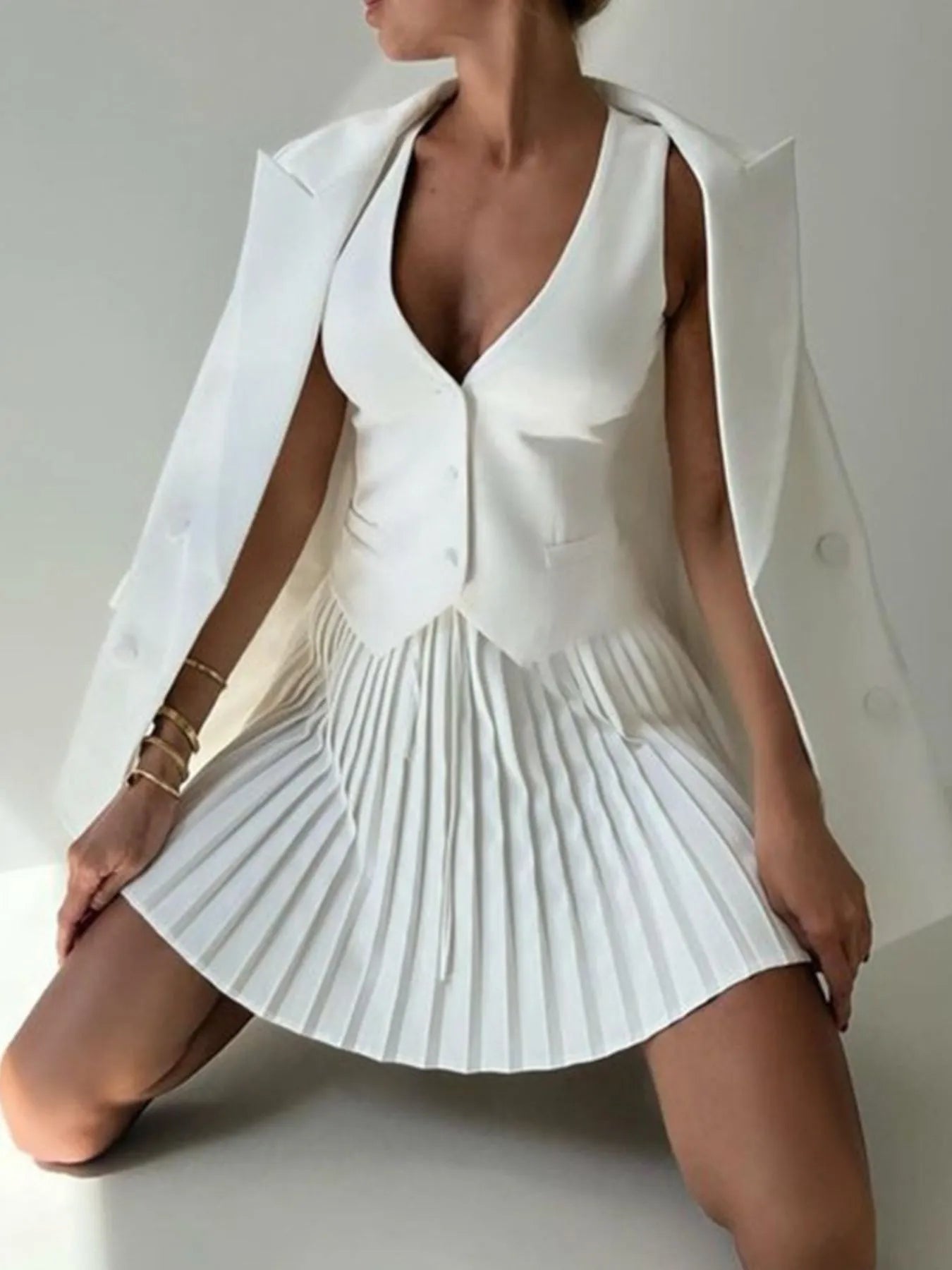 Woman wearing a white pleated dress with a cape over a plain background