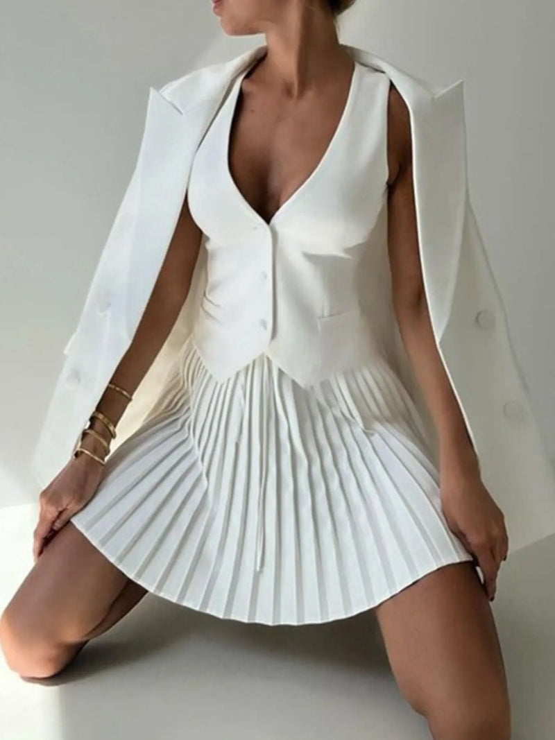 Woman wearing a white pleated dress with a cape over a plain background
