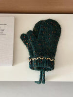 Green knitted baby bootie with beige trim on a white surface