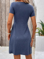 Woman wearing a blue dress standing against a wooden and white wall.