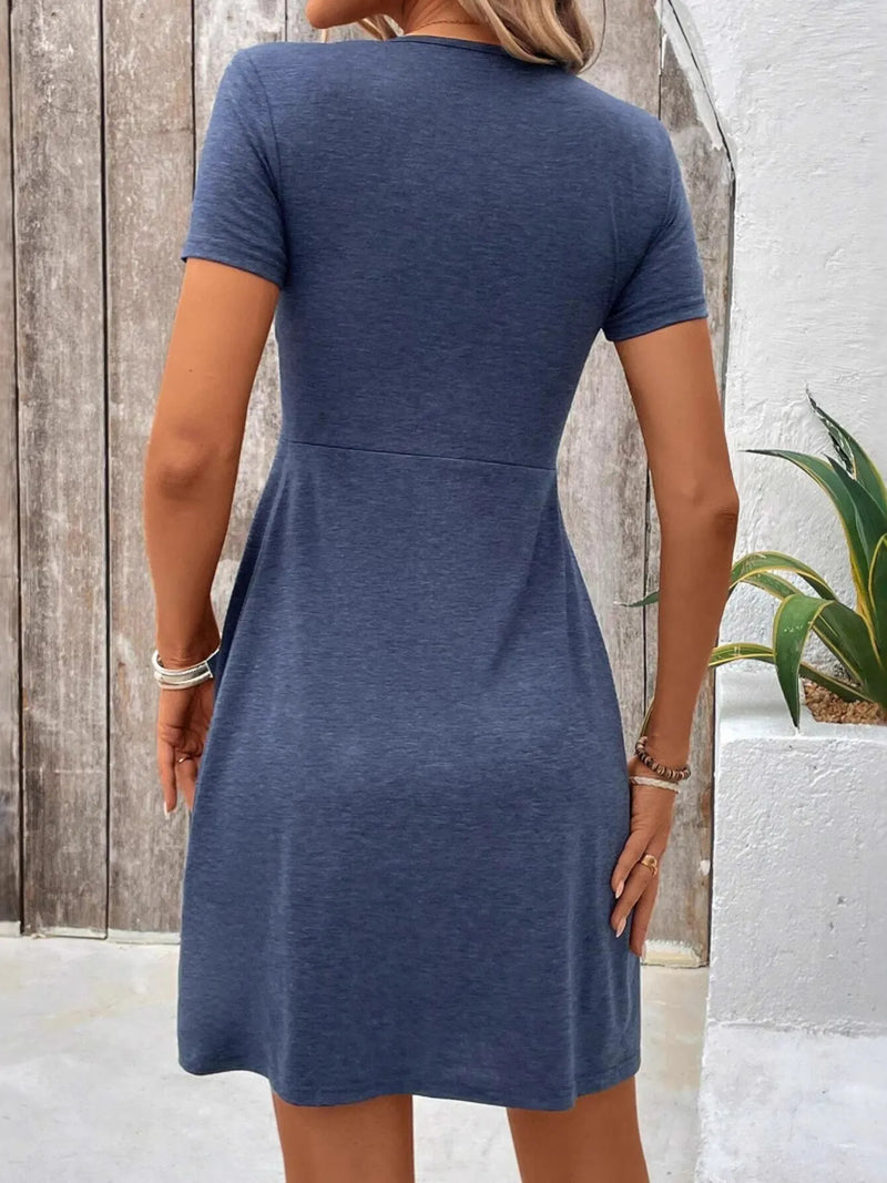 Woman wearing a blue dress standing against a wooden and white wall.