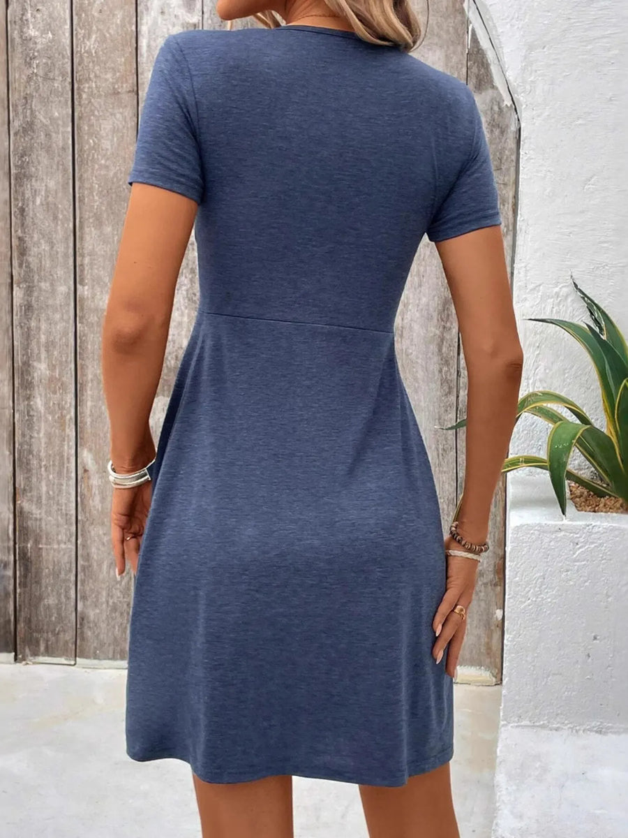 Woman wearing a blue dress standing against a wooden and white wall.