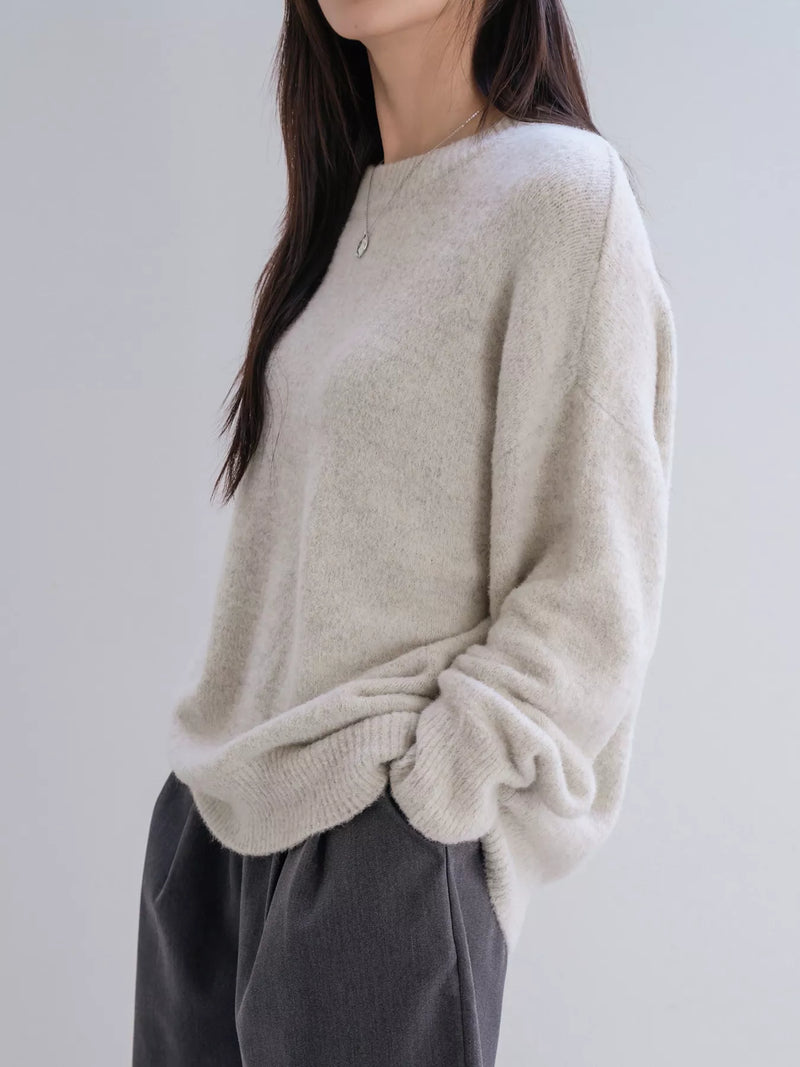 Person wearing a beige sweater and dark pants against a plain background