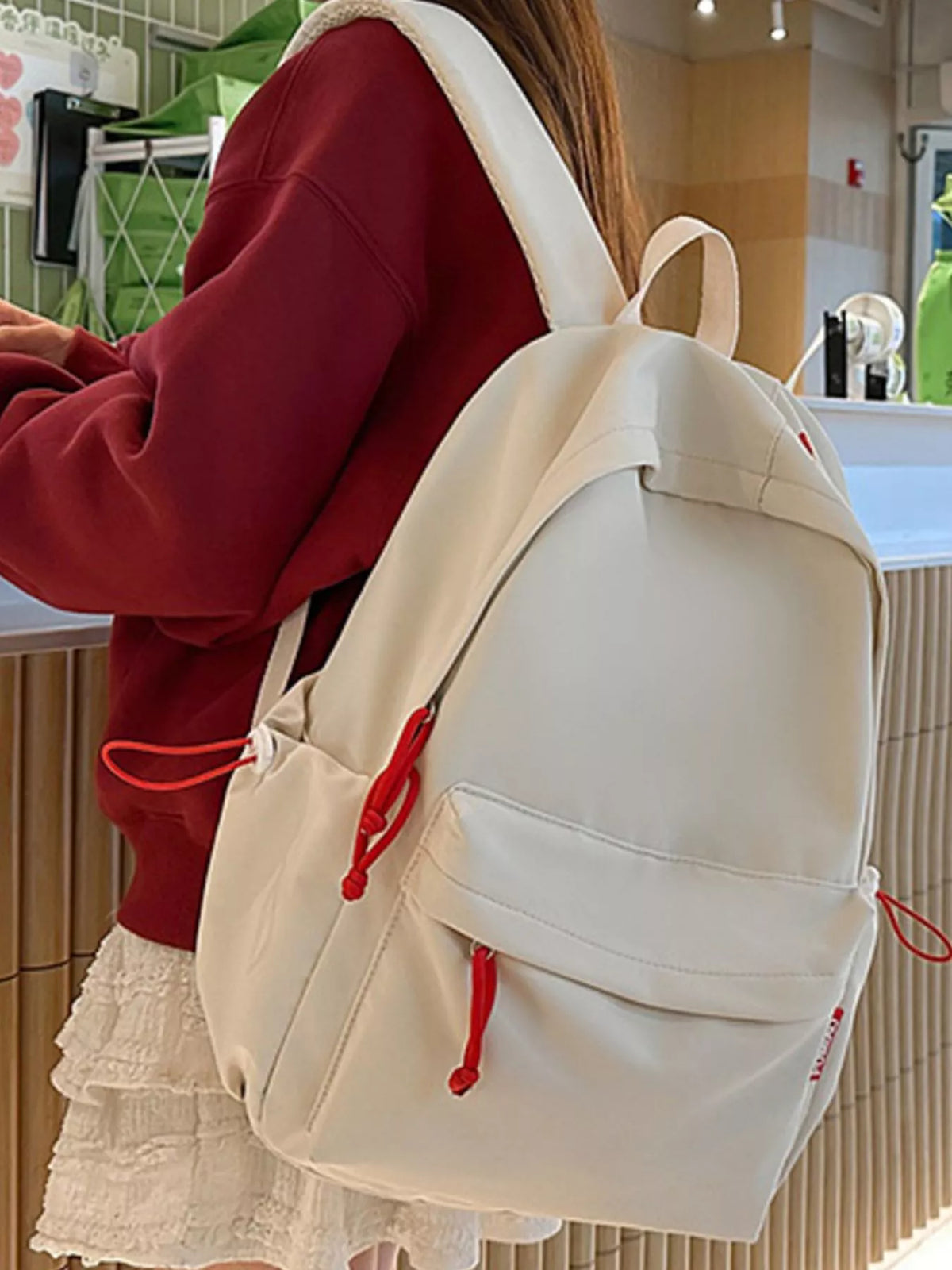 Person wearing a white backpack with red straps in an indoor setting