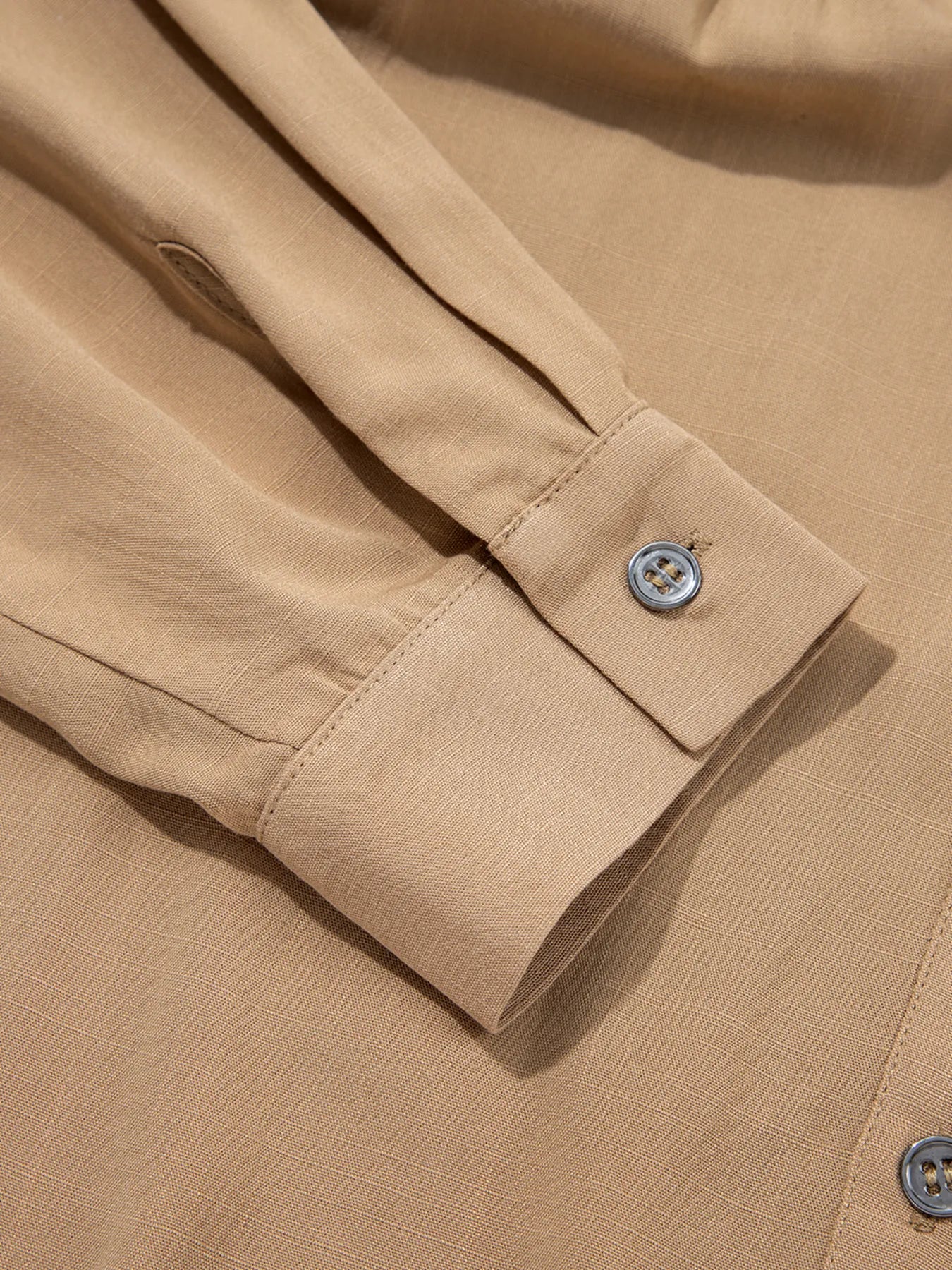 Close-up of a beige shirt with rolled-up sleeve and button detail