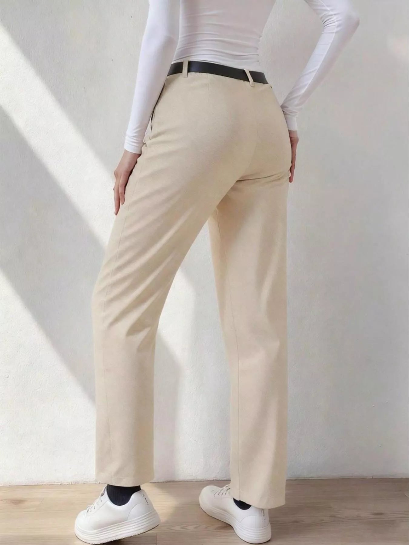 Person wearing beige pants and white sneakers in a minimalistic setting