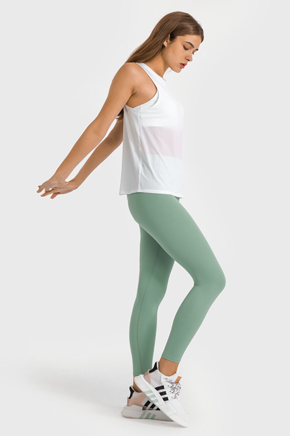 Woman wearing a white tank top and green leggings on a white background