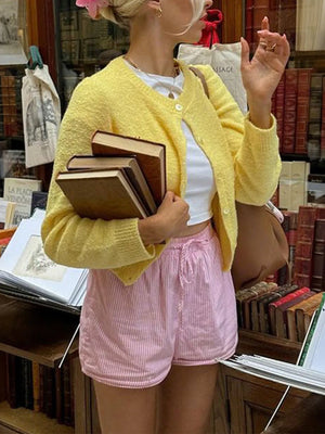 Person wearing a yellow cardigan and pink shorts holding books in a library setting