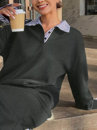 Person wearing a dark gray sweater with a striped shirt underneath, holding a coffee cup.