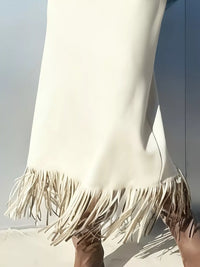 Close-up of a white dress with fringes held by a person against a light background
