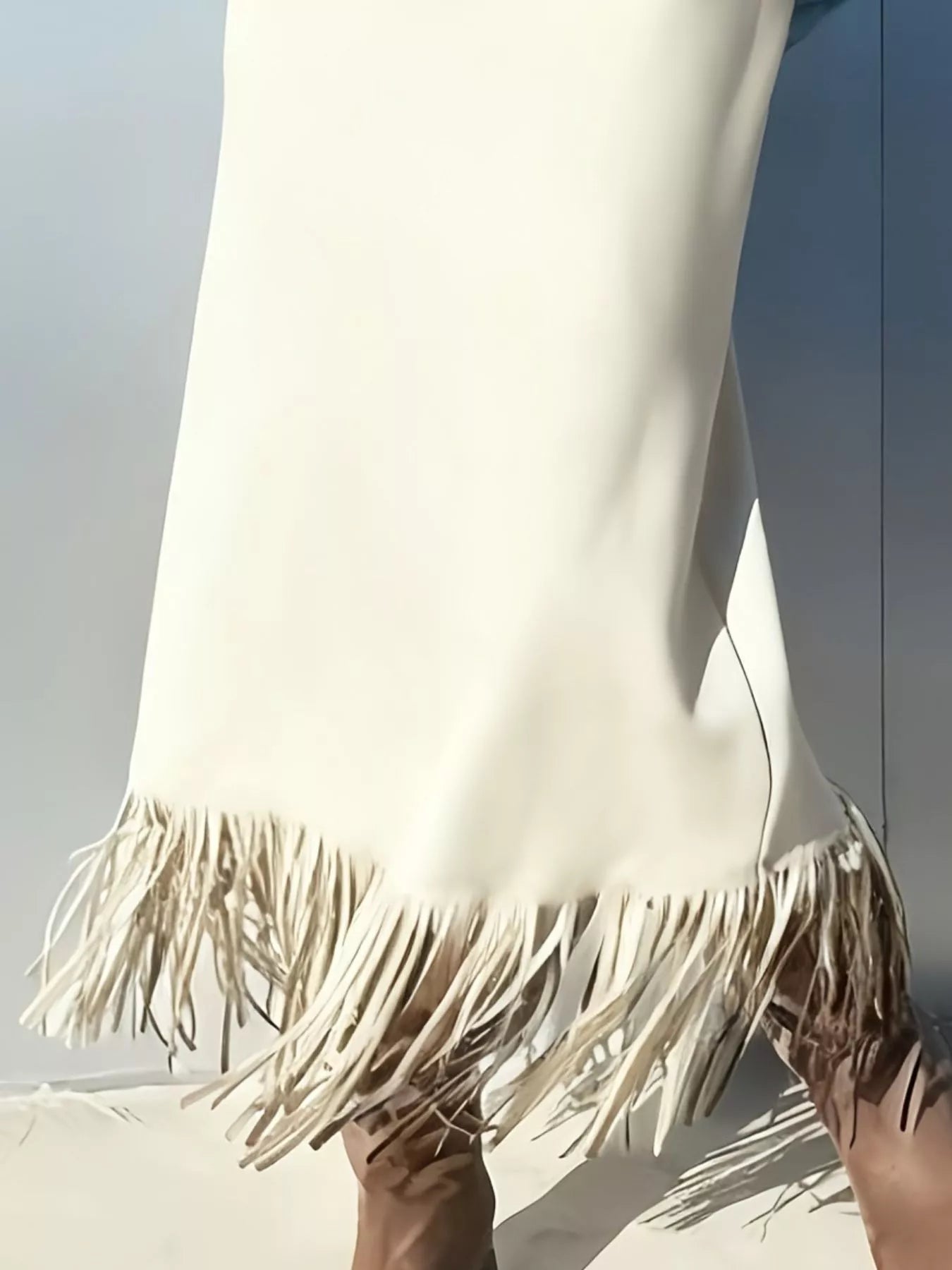 Close-up of a white dress with fringes held by a person against a light background