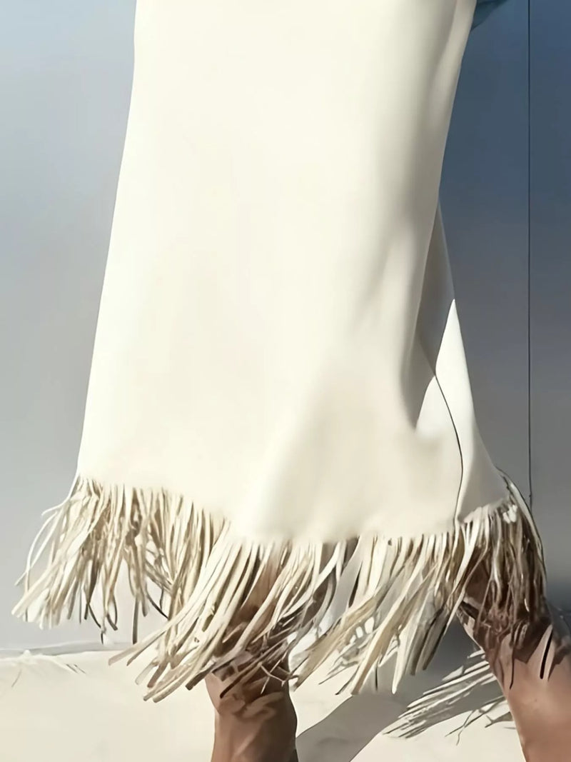Close-up of a white dress with fringes held by a person against a light background