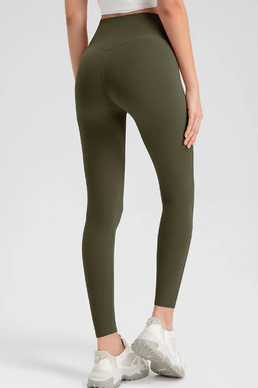 Person wearing olive green leggings and white sneakers on a white background