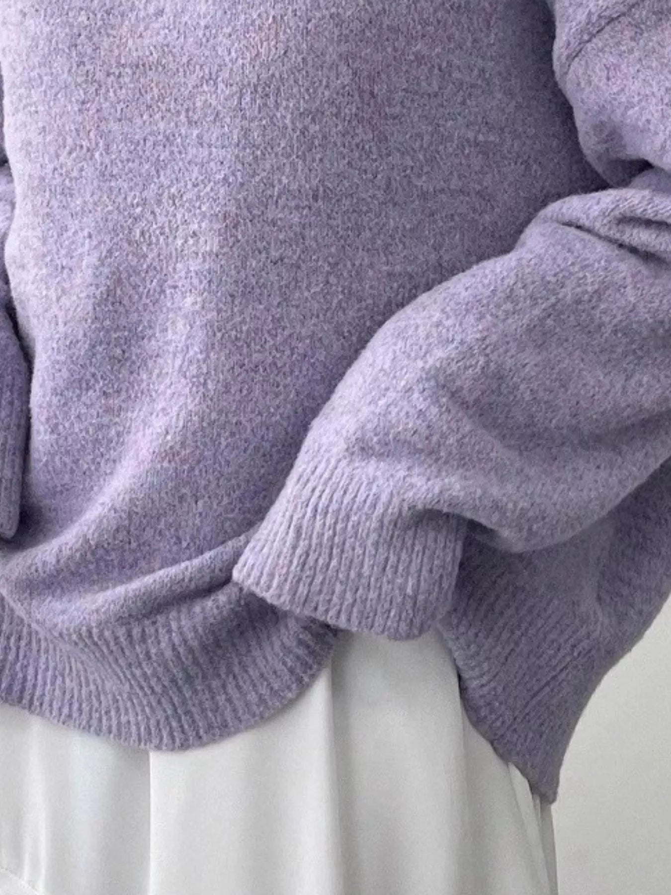 Close-up of a person wearing a light purple sweater with a neutral background