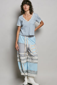 Woman wearing a light blue patterned top and patchwork pants on a plain background