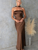 Woman wearing a brown halter neck dress against a textured wall with a vase of pampas grass.