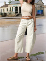 Person wearing a beige sleeveless top and white wide-leg pants on a street.