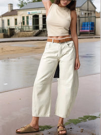Person wearing a beige sleeveless top and white wide-leg pants on a street.