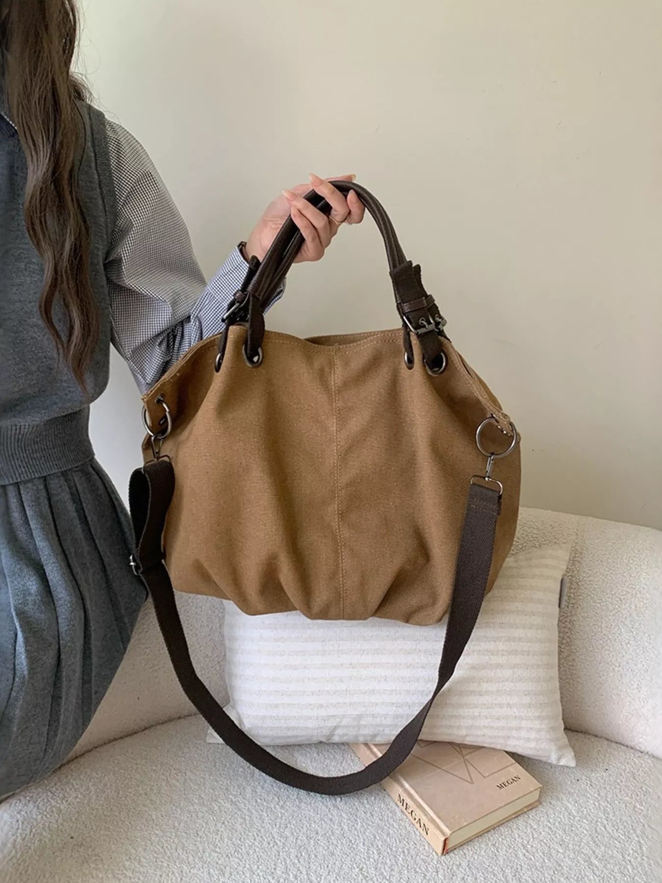 Person holding a brown handbag on a couch with a neutral background