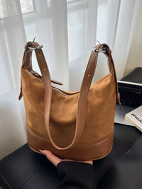 Brown suede handbag held by a person with a blurred indoor background