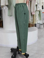 Green wide-leg trousers with an elastic waistband and a single black button on the left side, displayed on a dress form in a clothing store.