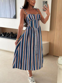 Woman taking a mirror selfie wearing a blue and beige striped dress in a modern room.