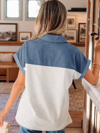 Woman wearing a blue and white color-blocked shirt in an indoor setting with framed pictures on the wall.