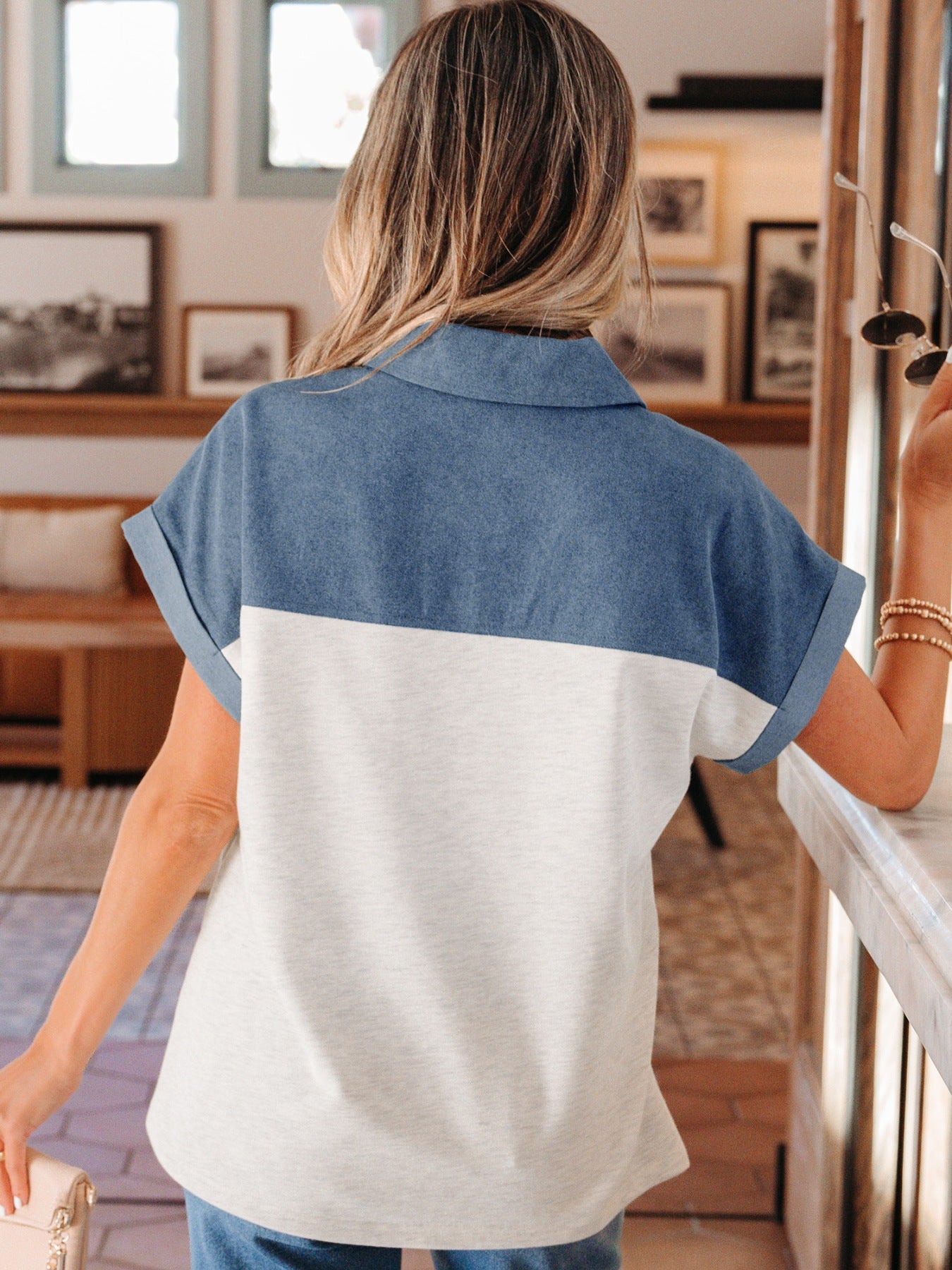Woman wearing a blue and white color-blocked shirt in an indoor setting with framed pictures on the wall.