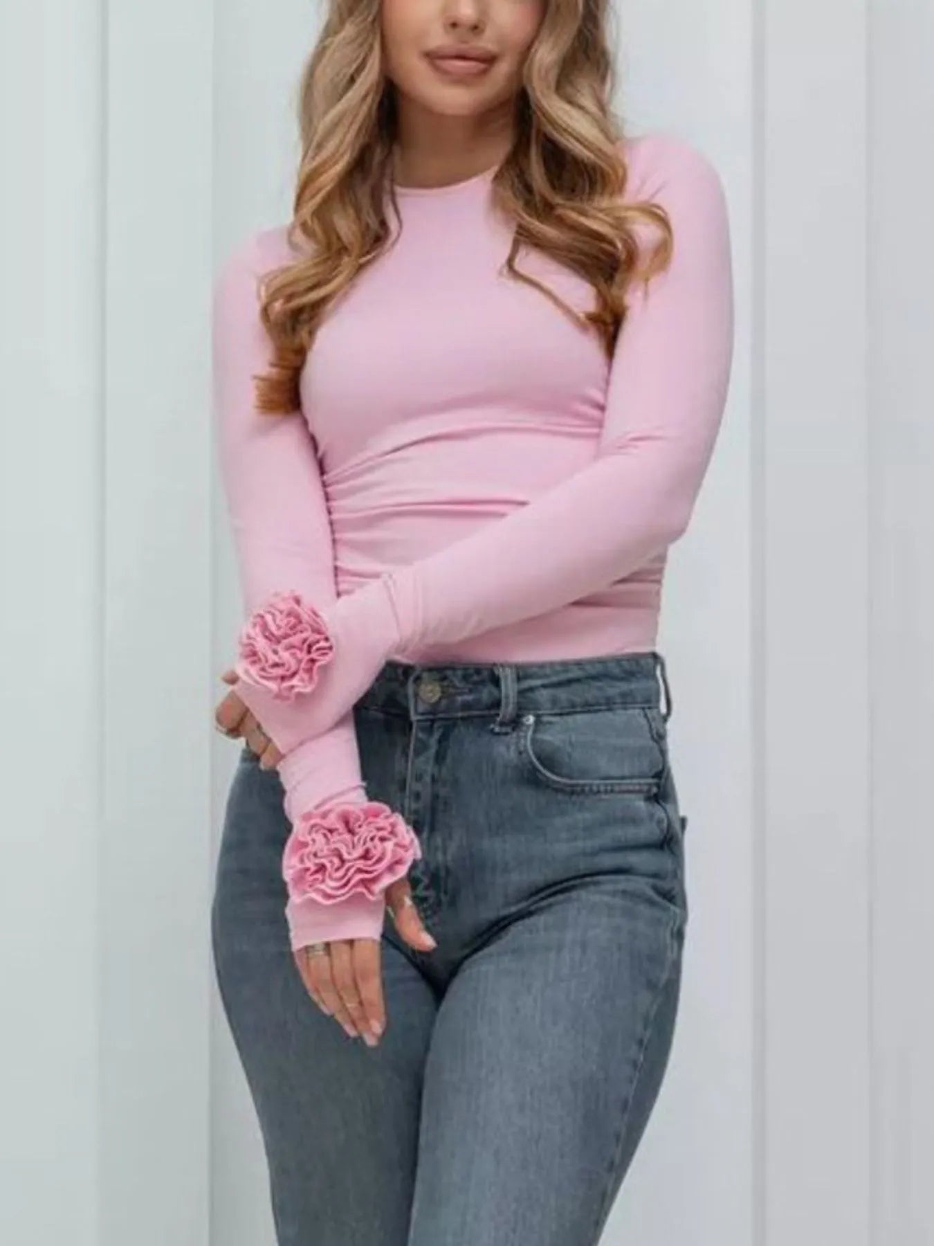 Person wearing a pink long-sleeve top with floral cuffs and blue jeans against a white background