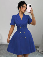 Woman wearing a blue dress with gold buttons, taking a mirror selfie.