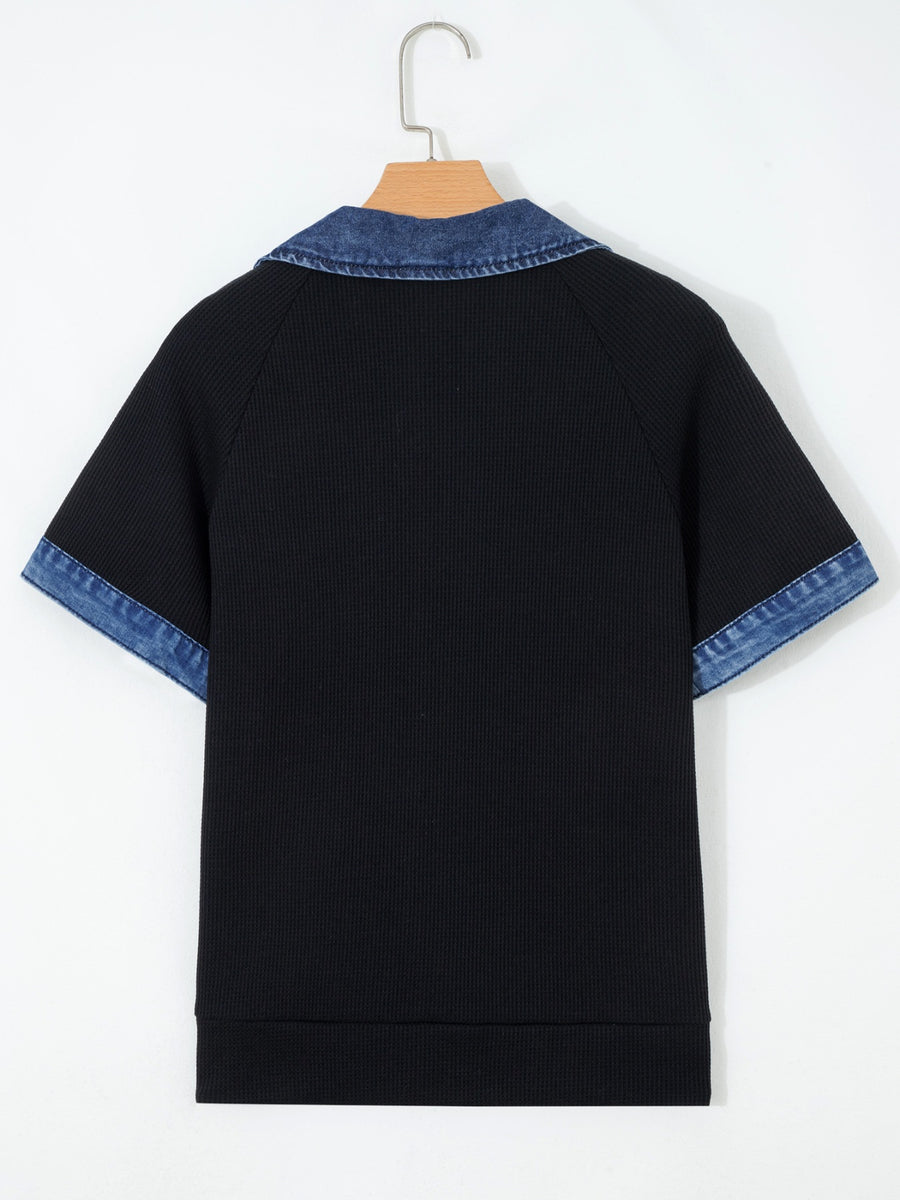 Black shirt with blue trim on a hanger against a white background