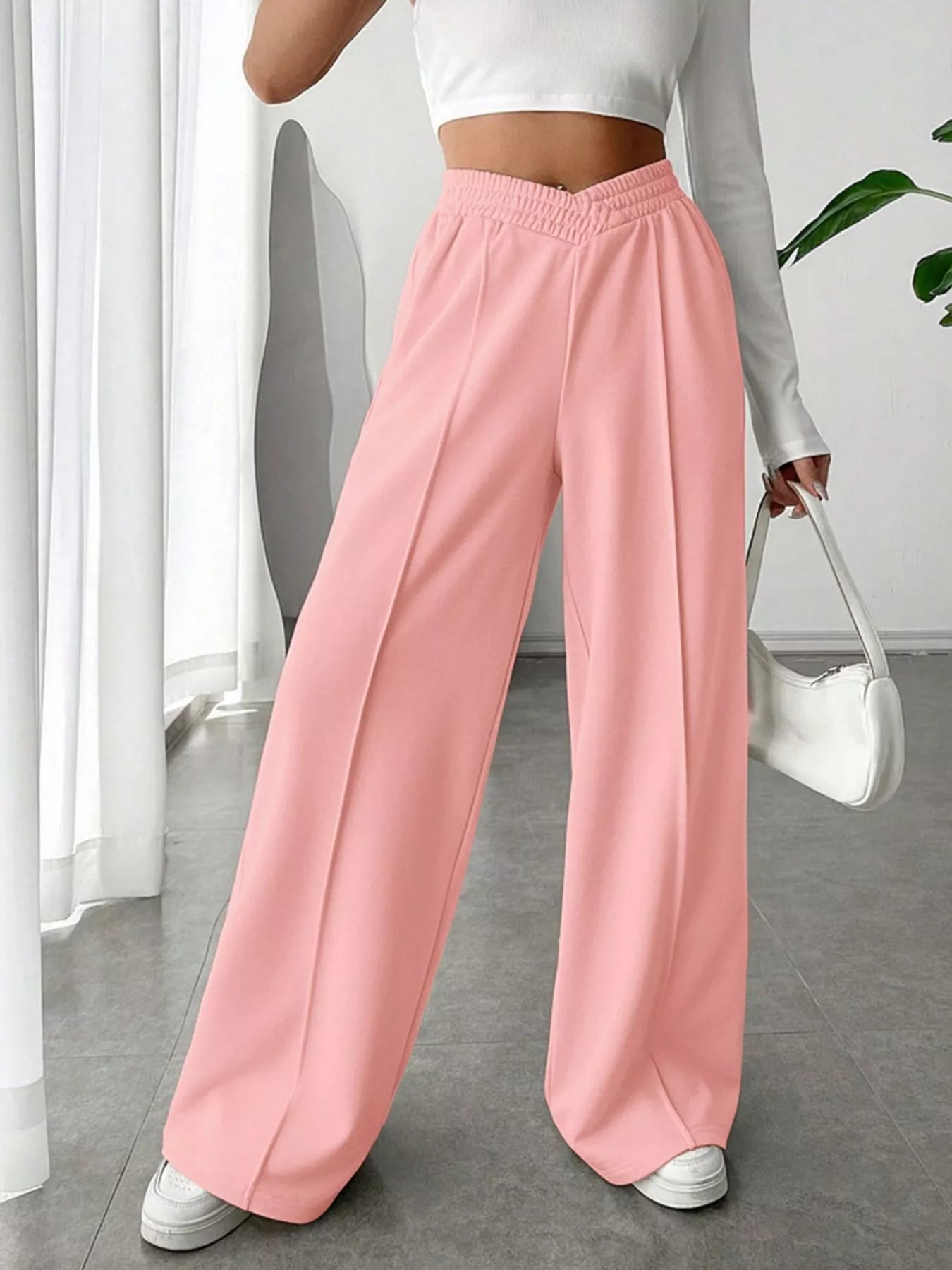 Person wearing pink wide-leg pants and a white top, holding a white handbag indoors.