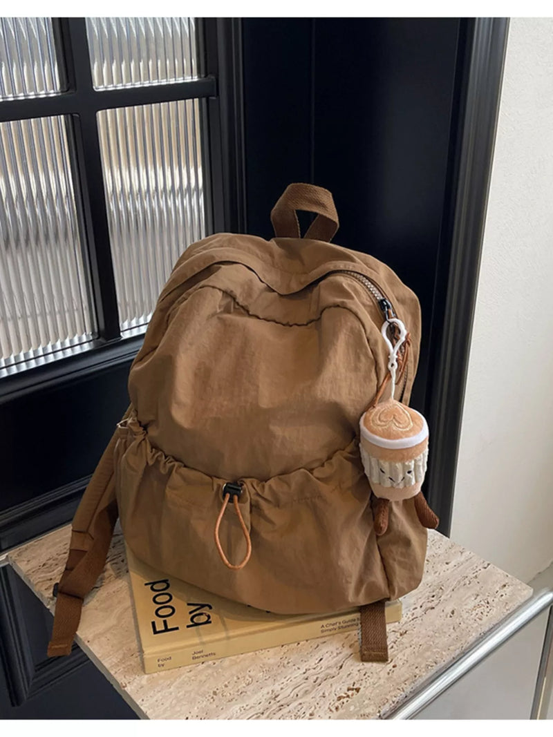 Brown backpack with a small round bag attached on a surface near a window.