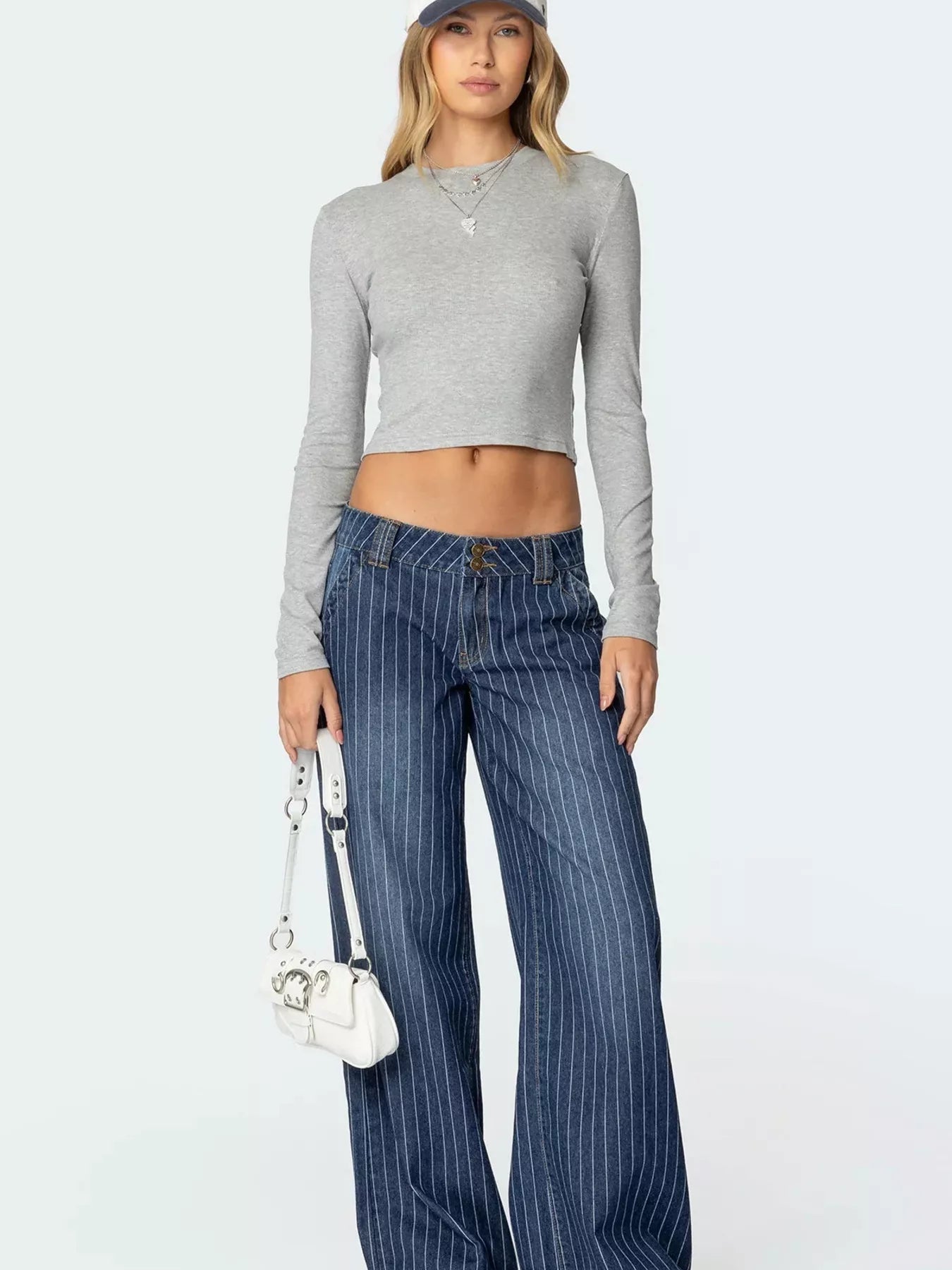Woman wearing a gray long-sleeve crop top and blue pinstripe pants on a white background
