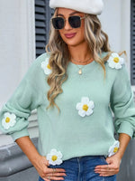 Woman wearing a light green sweater with white floral embellishments, standing outdoors.